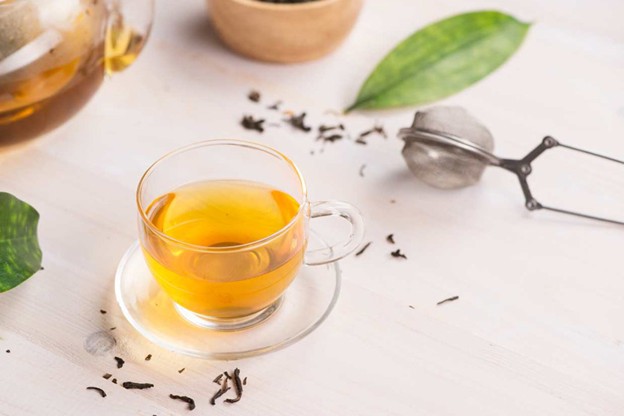 A cup of tea on a saucer next to a tea strainer
Description automatically generated